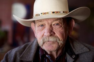 A older man wearing a cowboy hat and squinting at the camera.