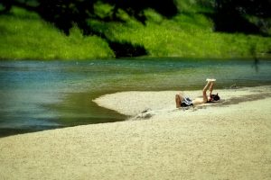 A person reading a book on the bank of a river.