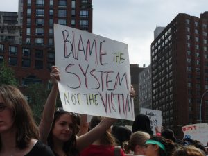 A protester holds up a sign: Blame the system, not the victim.