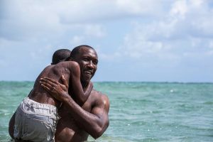 A still from Moonlight, featuring a Black man emerging from the ocean, holding a boy over his shoulder.