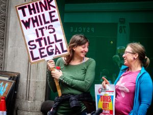 Protesters holding up a sign advising the viewer to think while it's still legal.