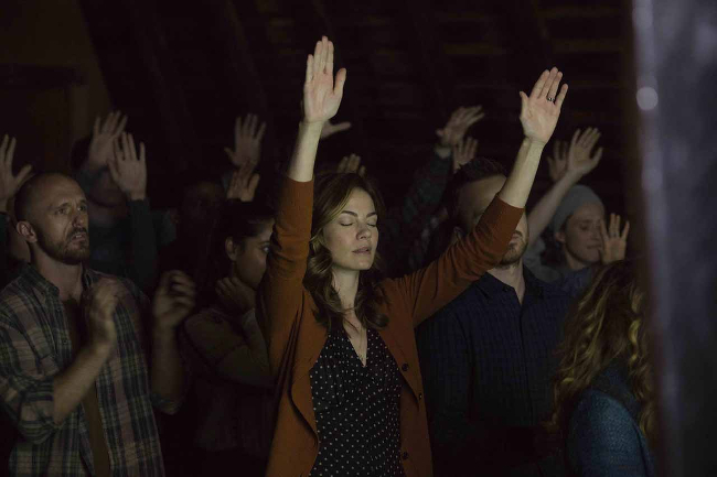 Worshipers raising their hands at a cult meeting in THE PATH