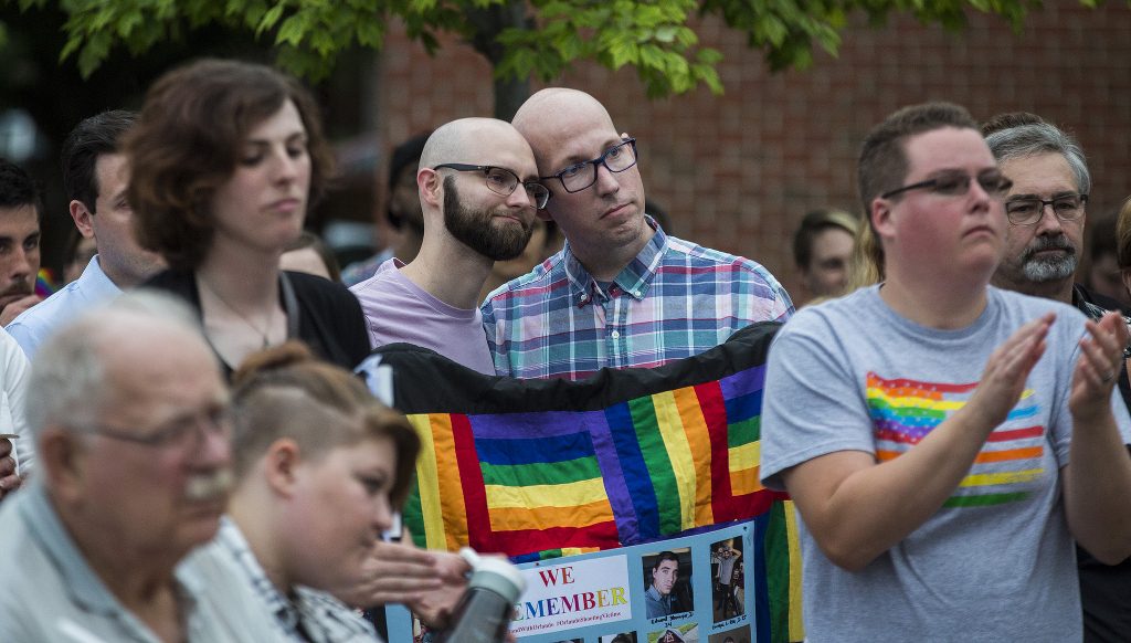 A gay couple leans on each other while listening to a speaker at a vigil for victims of the Pulse shooting.