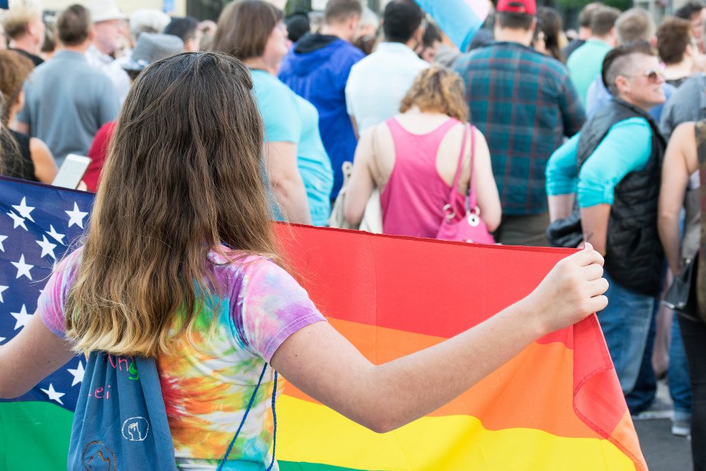 A young girl in tie-dye carrying a rainbow flag.