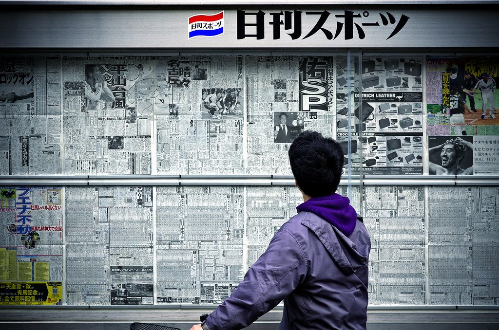 A Japanese person reading newspapers pasted on a wall.