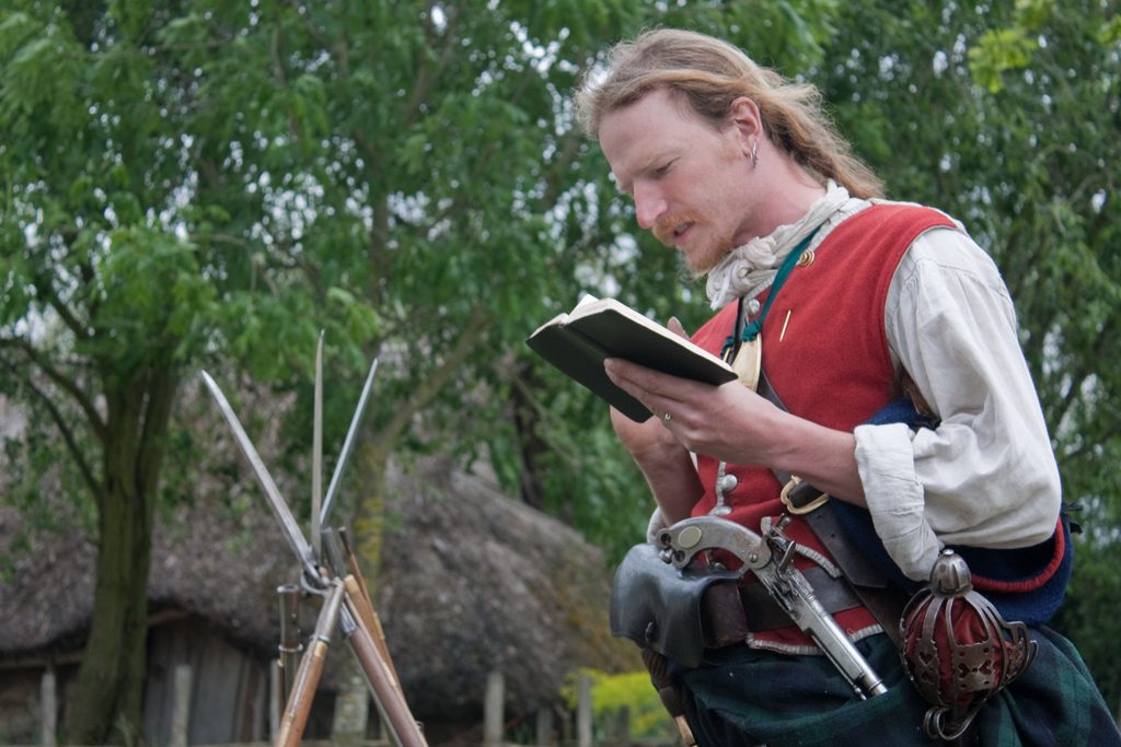 A man in historical costume reading a book.