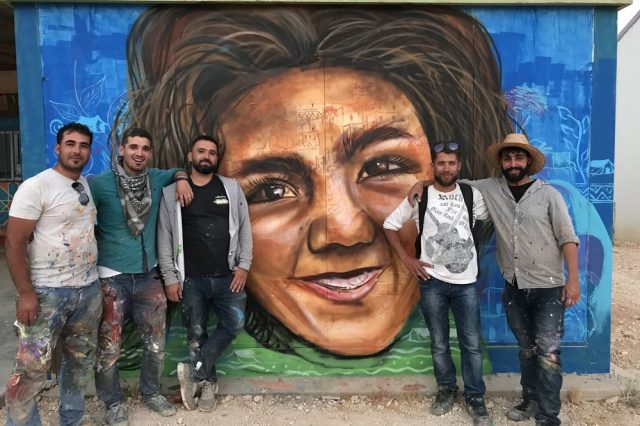 Refugees standing in front of a colourful mural